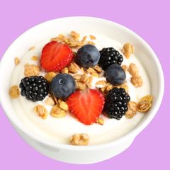 A white bowl of frozen yogurt topped with strawberry halves, blueberries, blackberries and granola